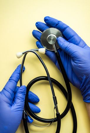 Top view of yellow table with hands wearing protective blue gloves holding stethoscope
