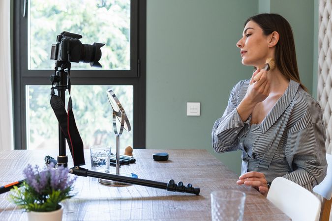 Happy woman applying powder and recording video on camera