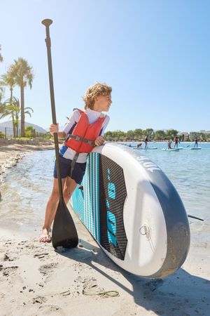 Boy with paddle leaning on SUP board and looking away