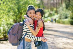 Two women hugging and looking at camera standing on walking path in park