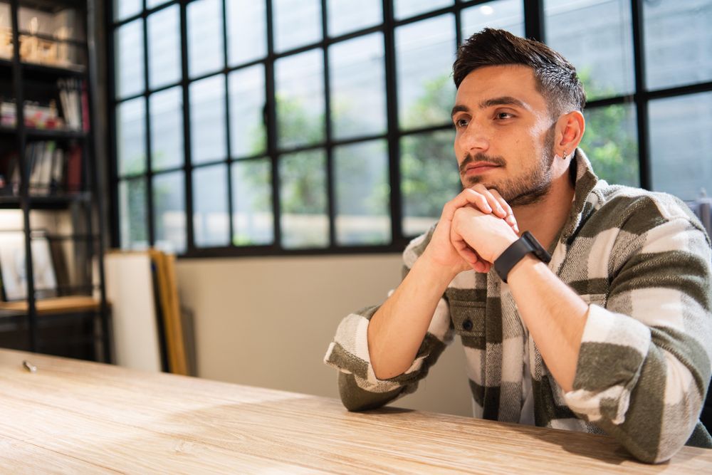 Man in bright office sitting at table deep in thought