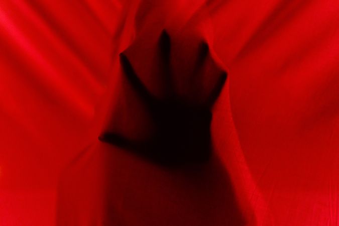 Faceless person hiding behind curtains at night time