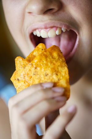 Mouth of girl biting into tortilla chips