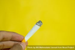 Yellow background with fingers holding lit hand rolled cigarette 5zrRqj