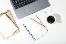 Top view of table with open laptop, earbuds, coffee, and blank notebooks