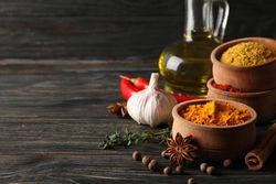 Turmeric in bowl with cinnamon sticks, garlic bulb and anise, copy space
