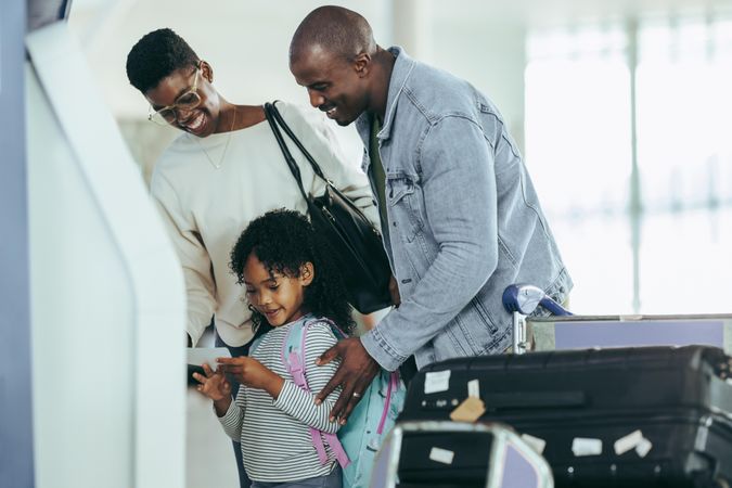 Black young girl with family reading boarding pass print from machine at airport