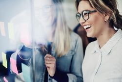 Two female colleagues laughing as they brainstorm with sticky notes