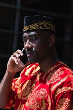 Black male in traditional clothes talking on cellphone in street