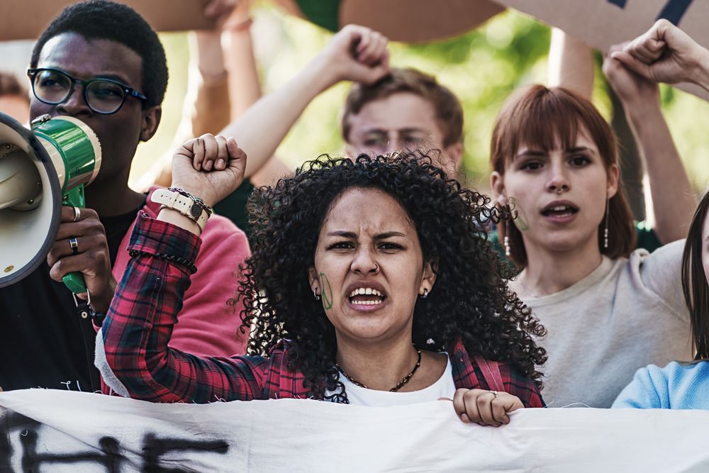 A curly-haired woman with a peace sign on her cheek, shouting and raising her fist