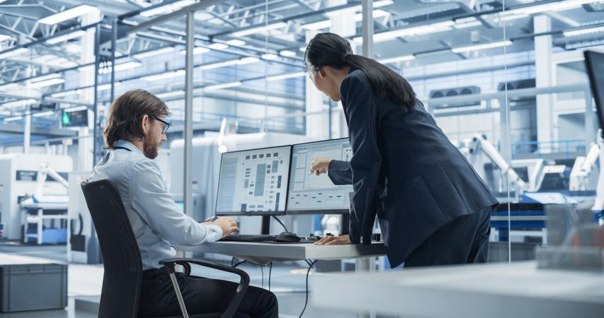 Handsome Engineer and a Beautiful International Business Manager Having a Conversation and Using Desktop Computer. Specialists Setting Up Production Values at an Electronics Assembly Plant