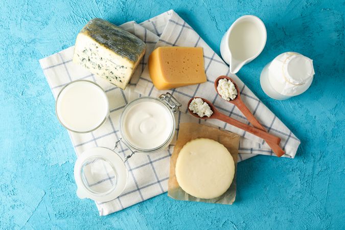 Fresh dairy products and kitchen towel on blue background, top view
