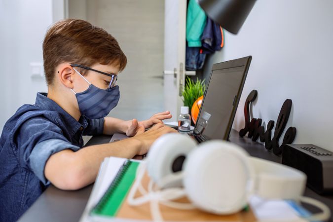 Teenager with face mask doing homework with laptop