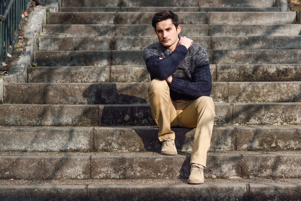Man in woolen sweater sitting on steps outside thinking with shadows of trees