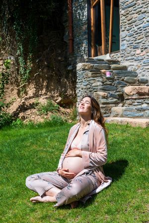 Happy pregnant woman enjoying the sun while sitting on the grass
