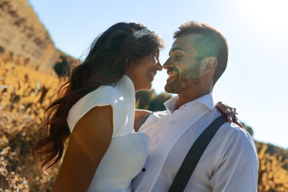 Newlyweds embracing in field with sun flare