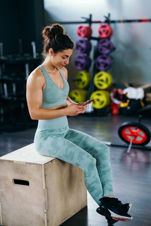 Woman texting on her phone in between workout, vertical