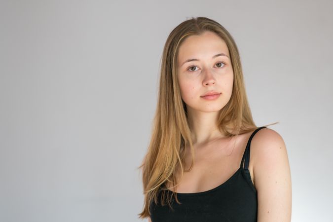 Portrait of blonde teenage girl in dark strap top against light background