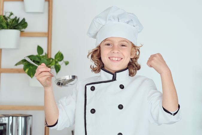 Cheerful boy in uniform with ladle in kitchen