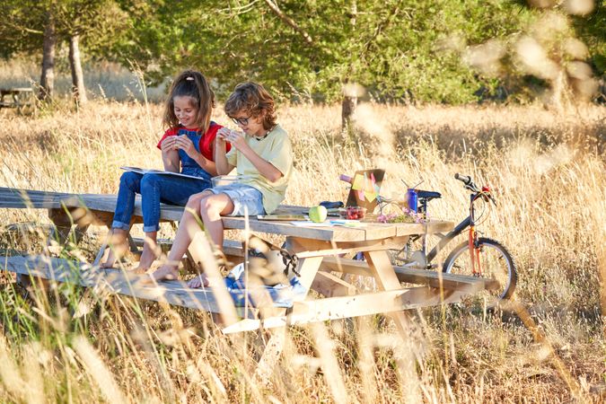 Cheerful children sitting on bench with book and sandwich