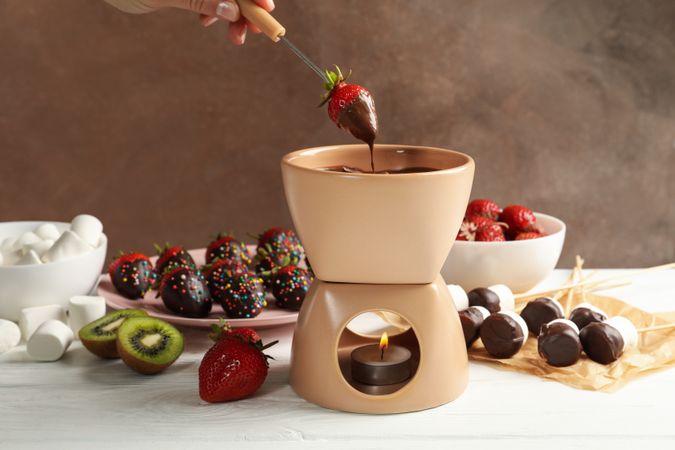 Woman dipping strawberry in chocolate. Delicious chocolate fondue