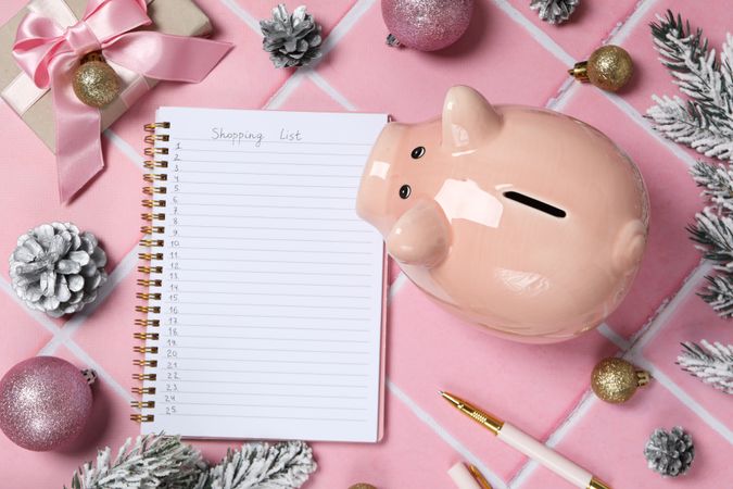 Piggy bank, Christmas decor and notepad with list on pink background, top view