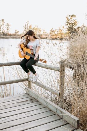 Young woman playing guitar near water