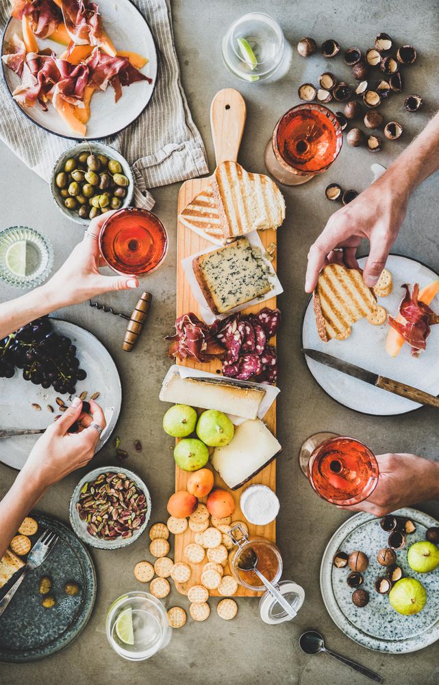 Charcuterie board with hands holding glass of rose and toasted bread