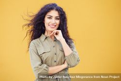 Female in army green jumpsuit smiling in front of mustard wall with hand to her chin 5kYWDb