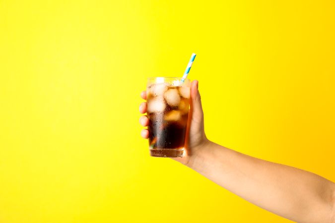 Female hand holding a glass with ice cola and tubule