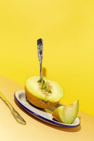 Sliced small melon on plate with spoon and fork