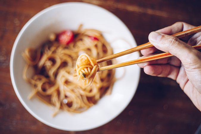 Faceless person eating dinner with chopsticks