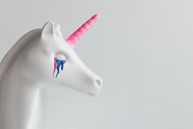 Painted unicorn head with pink horn and rainbow tears on bright background