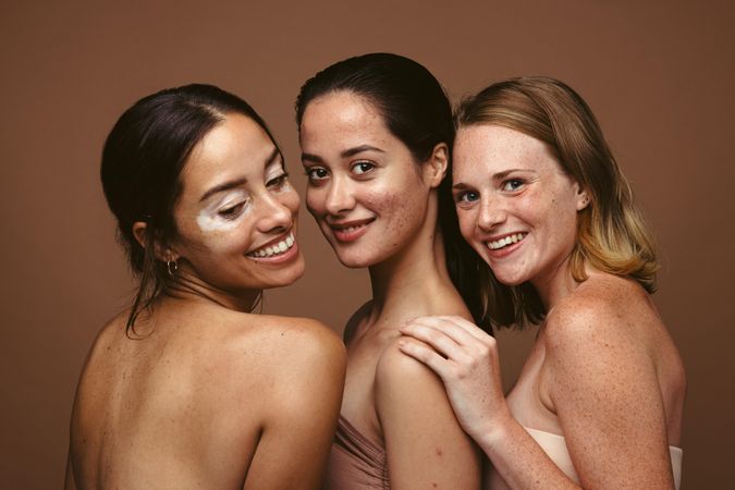 Group of women with skin conditions standing together on brown background