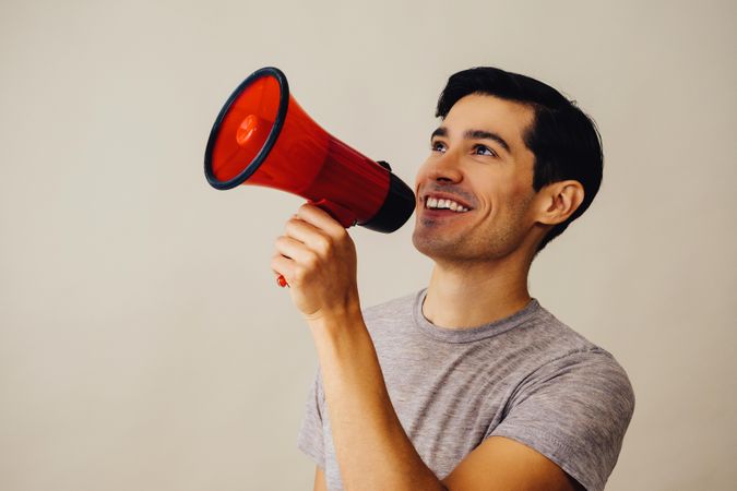 Side view of Hispanic male holding up red loudspeaker