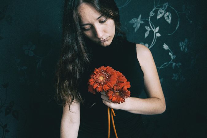 Studio portrait of woman with holding gerbera flowers against floral wall