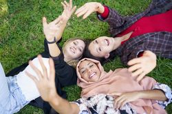 Looking down at three friends lying on grass taking photo with smartphone