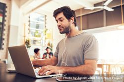 Portrait of a young man with earphones using laptop at a cafe 5kjRj0
