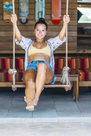 Cheerful woman riding on swings on tropical terrace
