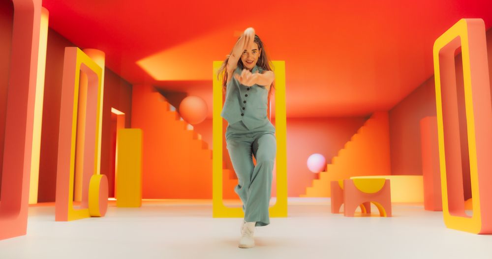 Portrait of Young Woman Sitting in Geometric Abstract Environment, Dancing with Hypnotic Graceful Movements. Static Camera Capturing Fashionable Female Dancer in Colorful Studio