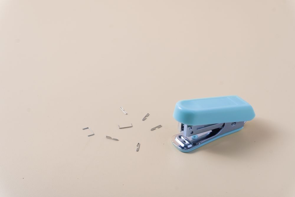 A desktop stapler surrounded by scattered staples on a table