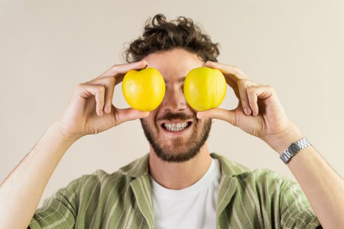 Funny young man holding two fresh apples over his eyes.