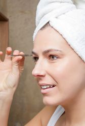 Portrait of woman plucking eyebrows with tweezers