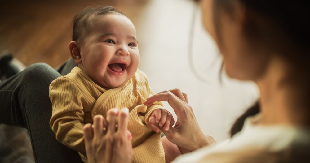 Portrait of a Cute Asian Baby Laughing, Resting on Her Mother's Lap and Enjoying a Bonding Time Together