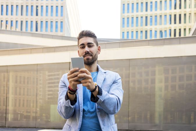 Smiling man in blazer leaning on pole outside taking a selfie