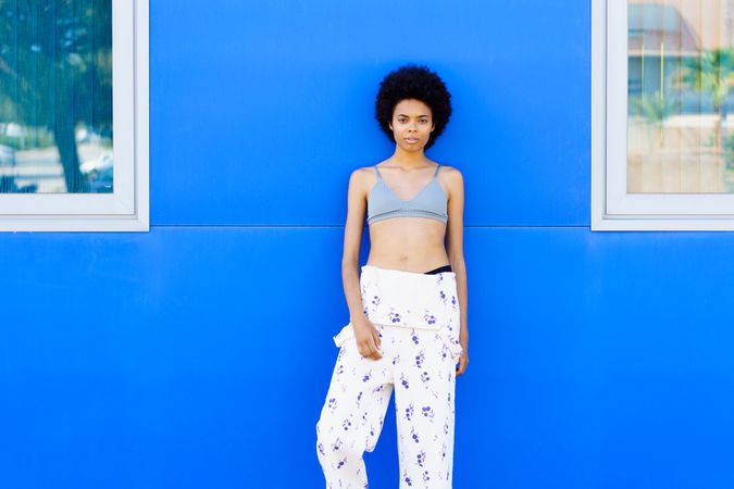Woman in floral coveralls looking at camera while leaning against blue outdoor wall
