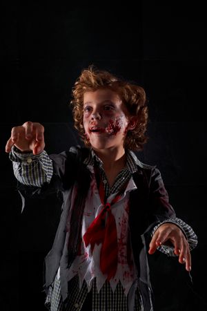 Vertical photo of a child disguised as a zombie with blood and glitter with arms raised walking