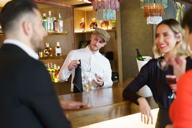Bartender polishing glassware with guests at bar