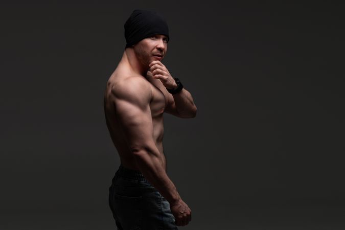 Muscular man in beanie posing shirtless, strong gaze.