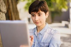 A Young Woman Engaged in Using a Tablet While Enjoying an Outdoor Setting in Daylight